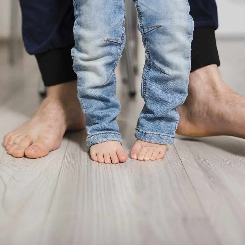 Barfüße eines Kindes stehen zwischen den Füßen des Vaters auf einem Holzboden