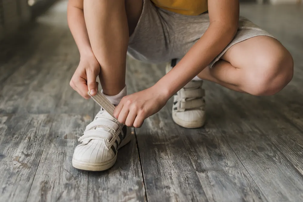 Kind schließt im Hocken den Klettverschluss seiner weißen Turnschuhe