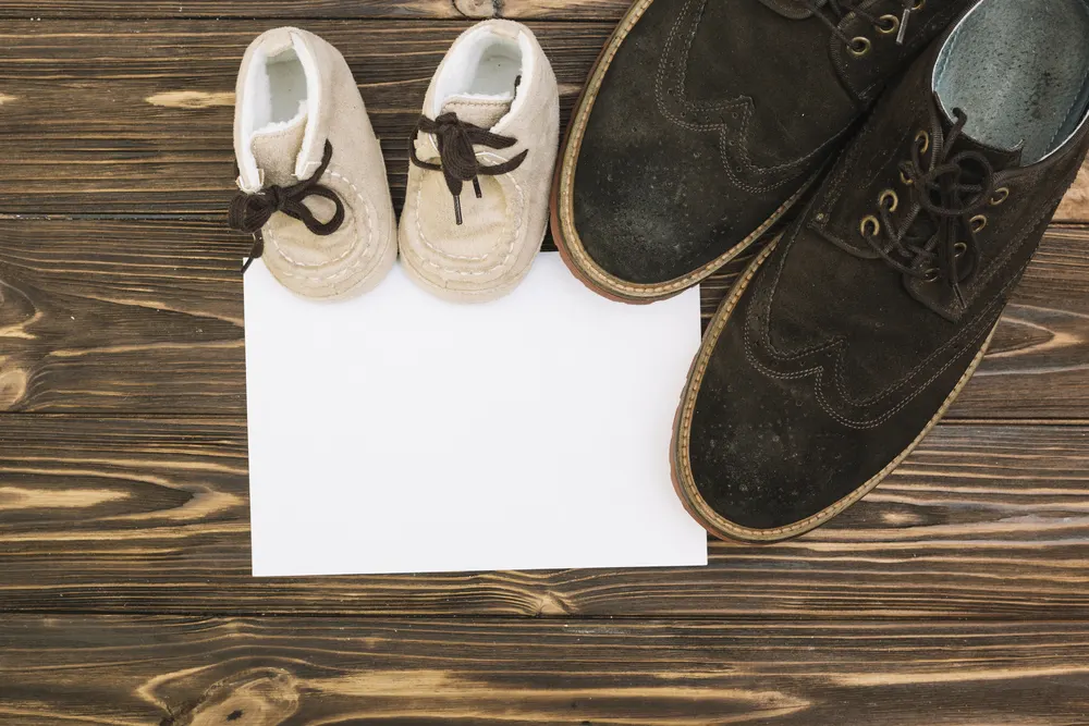 Kleine Kinderschuhe und große Lederschuhe neben einem leeren Blatt Papier
