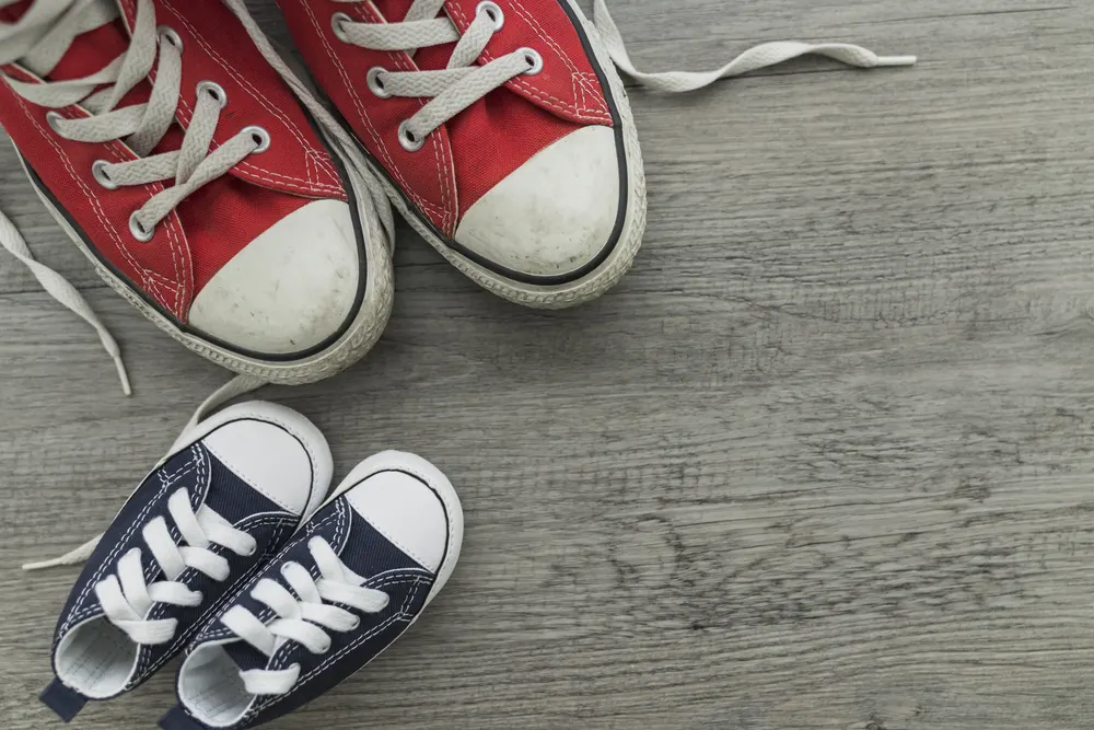 Kleine Kinderschuhe neben großen roten Turnschuhen auf einem Holzboden